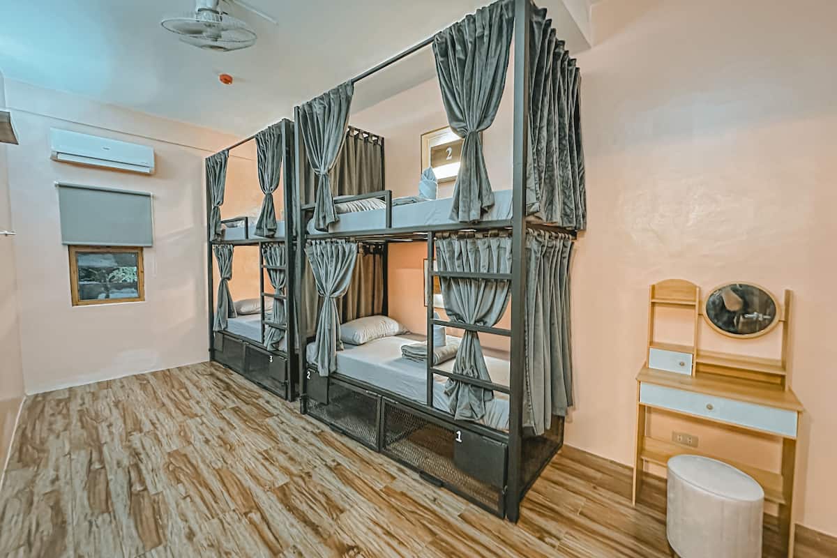 A bunk bed room with curtains, a small table, a mirror, and a ceiling fan.