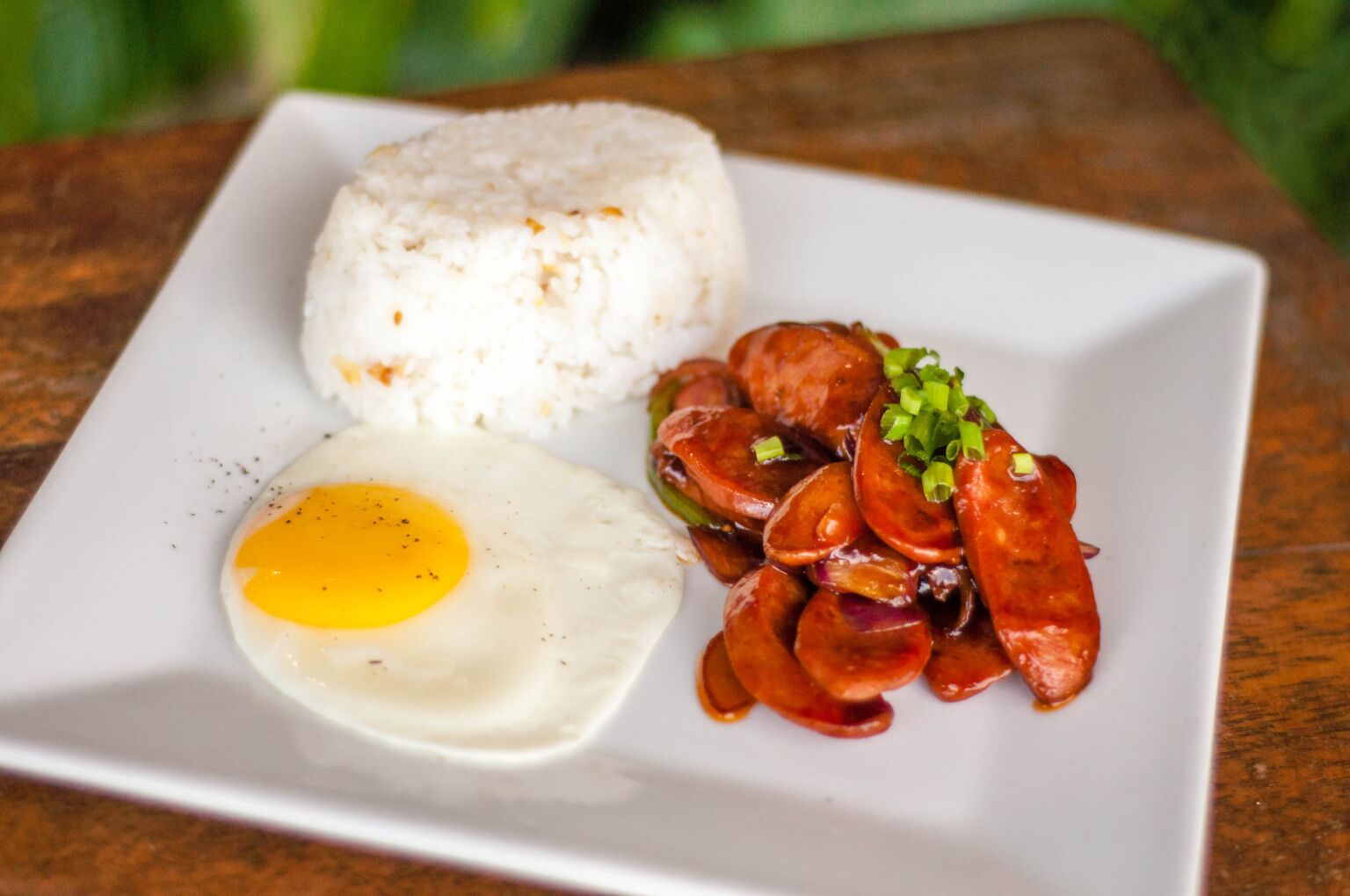 Um prato com arroz branco, um ovo frito e um acompanhamento de linguiça.