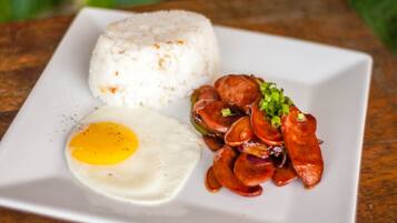 Um prato com arroz branco, um ovo frito e um acompanhamento de linguiça.
