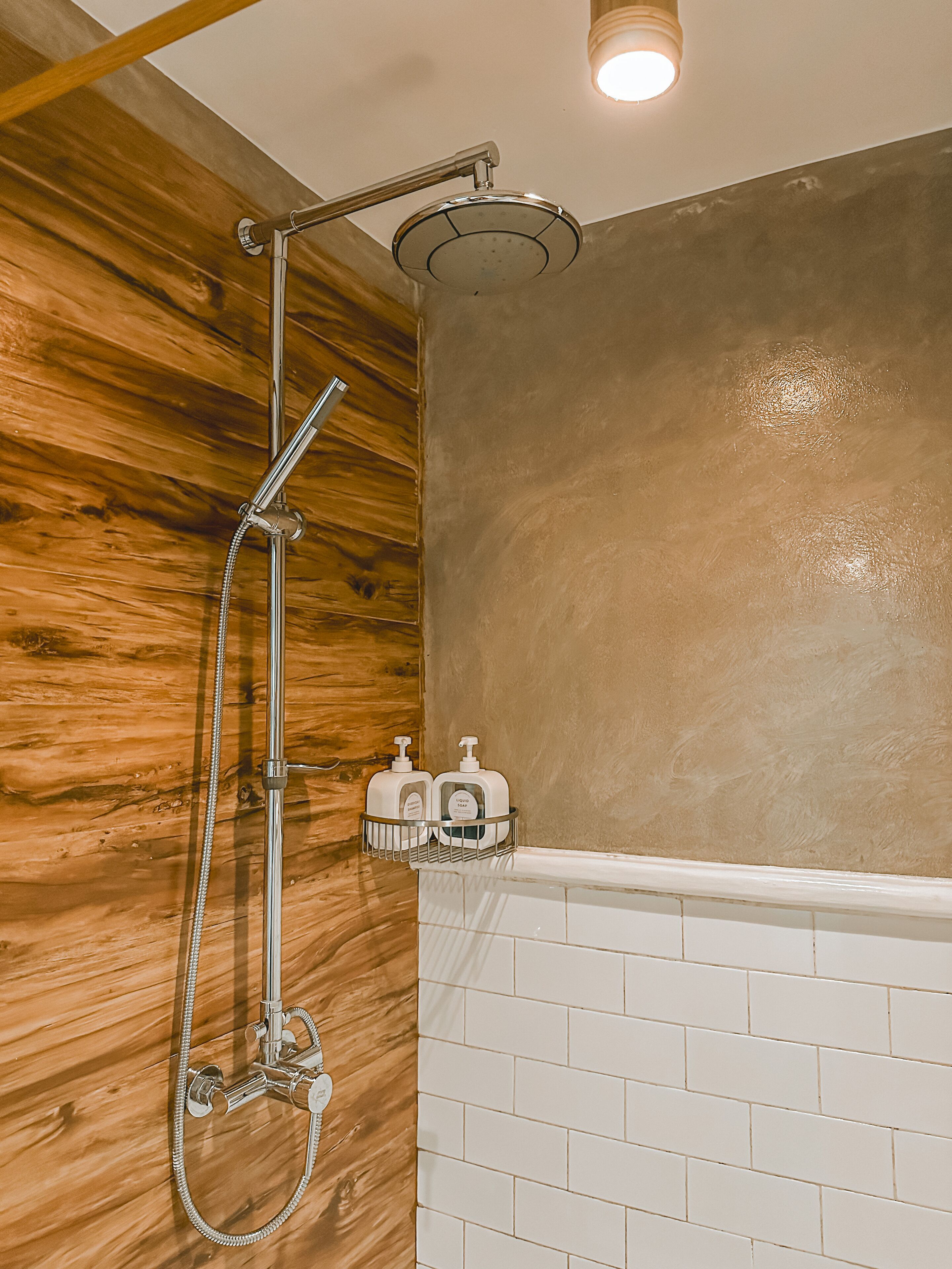 A shower with a wooden wall and a white tiled floor.