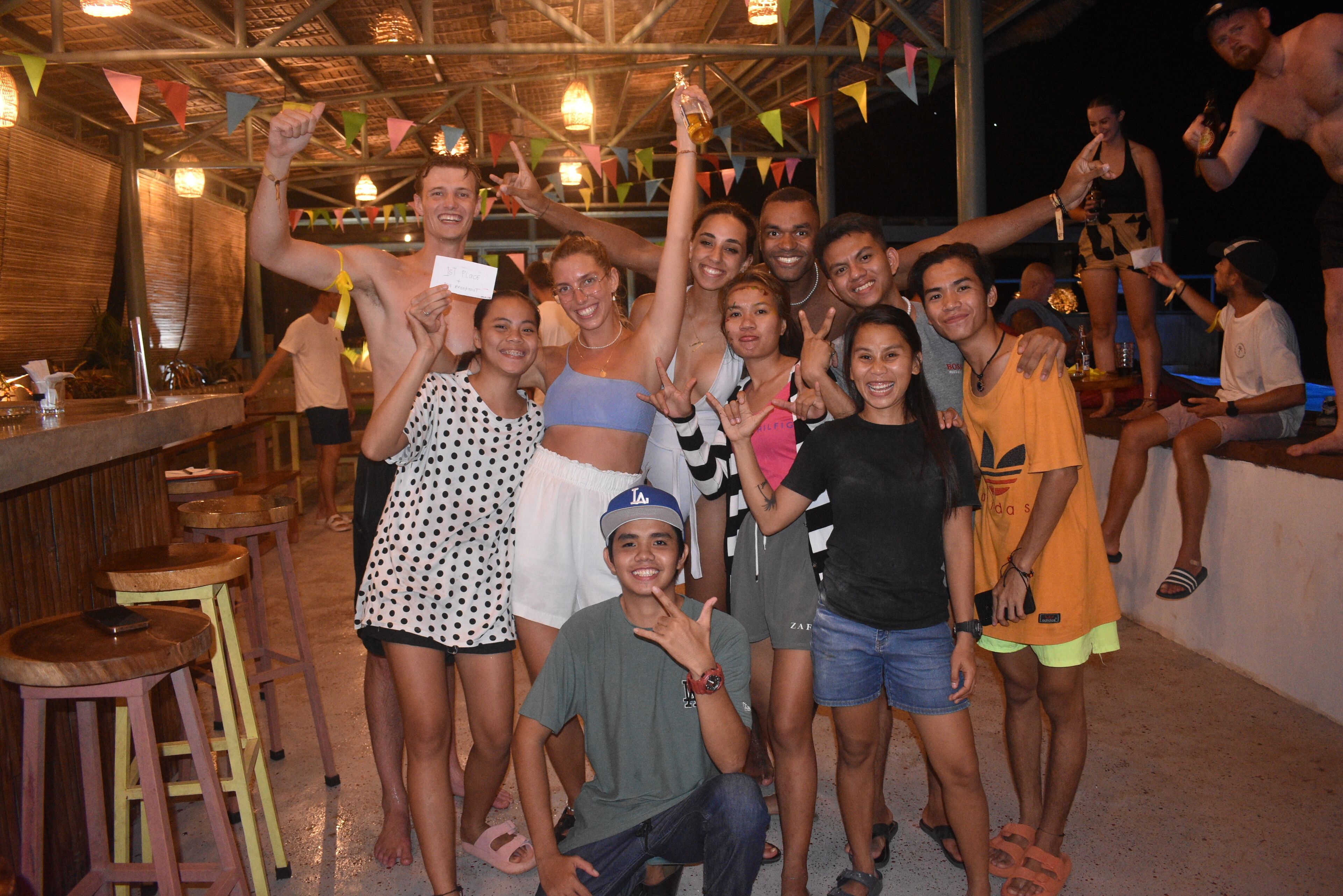 A group of people posing at a bar area with stools and a counter.