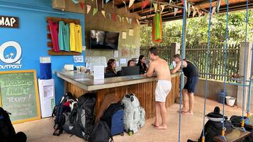 A beachside bar with a wooden counter, various flags, and a chalkboard sign.