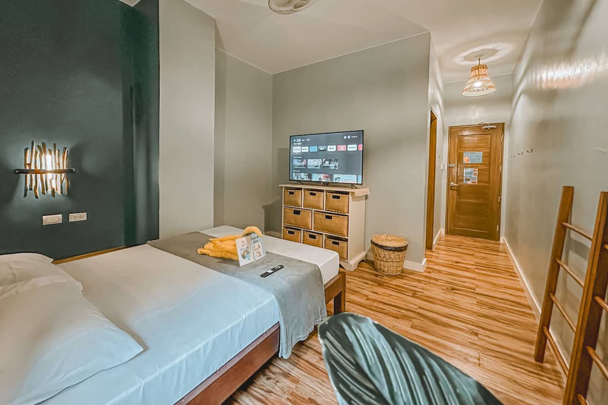 A hotel room with a bed, a TV, a wooden dresser, and a small table.