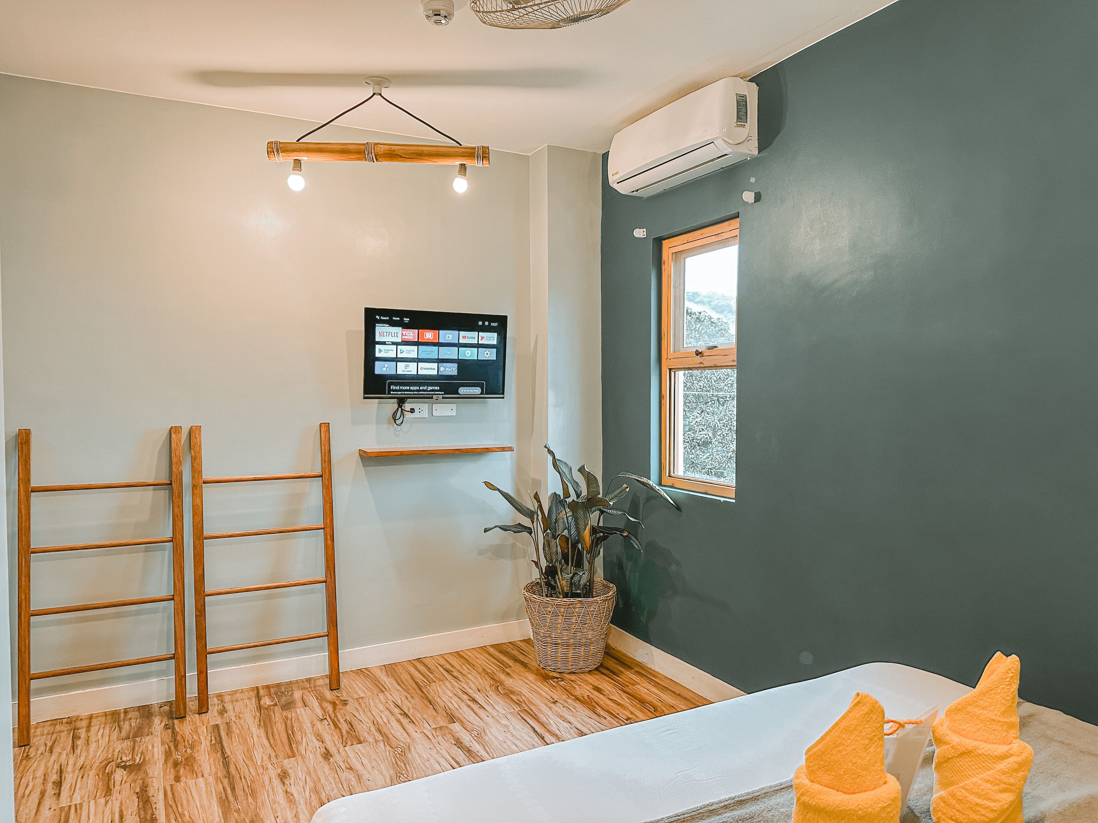 A room with a wooden ladder, a mounted TV, a window with a view, and a plant.