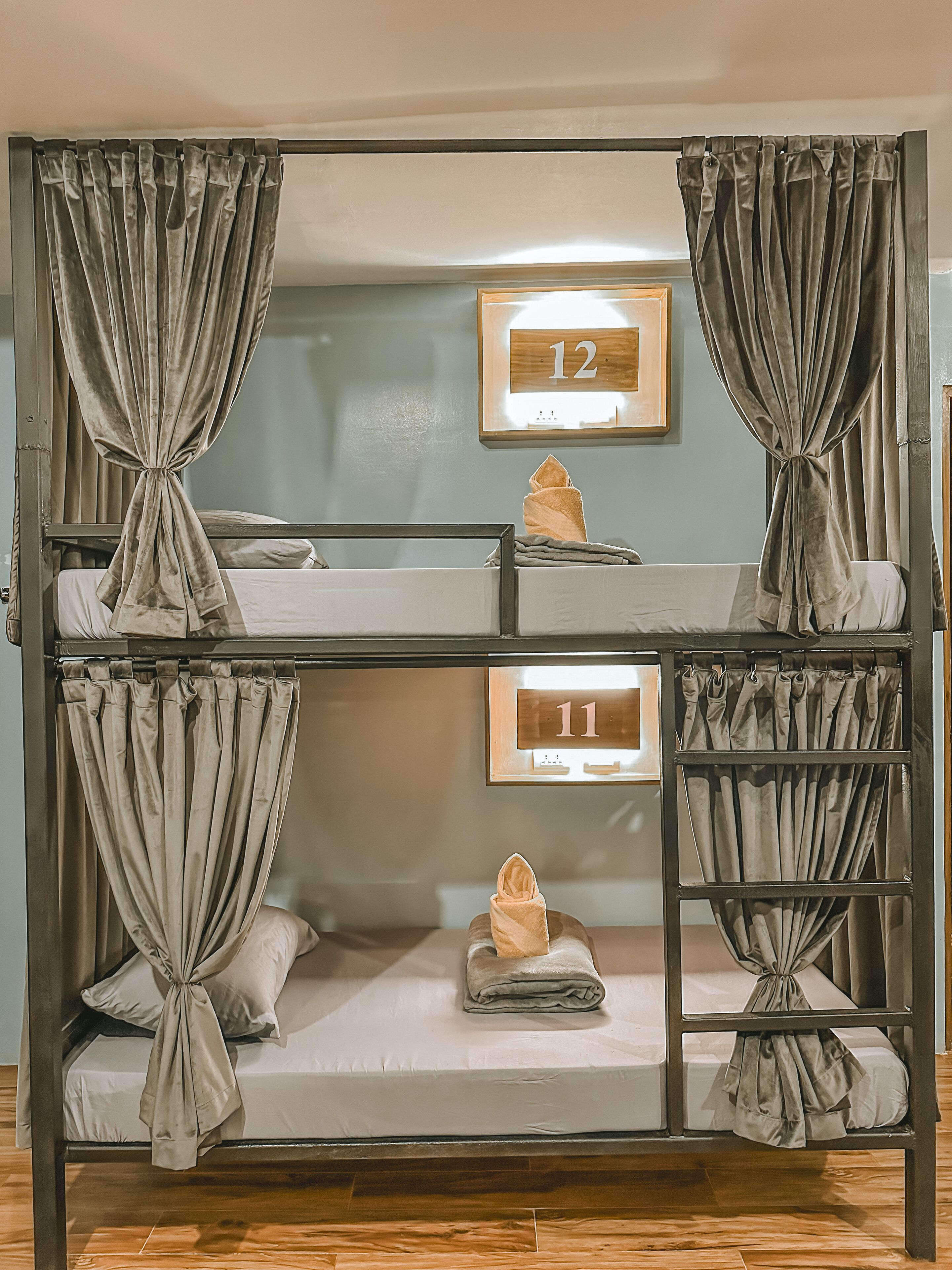 A bunk bed with curtains, a wooden number sign, and a folded towel on the lower bunk.