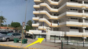 Ein mehrstöckiges Gebäude mit Balkonen, einem Parkplatz und einer Straße mit Autos und Palmen.