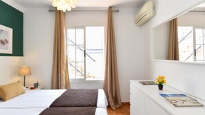 A hotel room with a bed, bedside table, lamp, air conditioning unit, window with curtains, and a dresser with a mirror. - Jacuzzi Garden Holiday Home (Playa del Inglés)