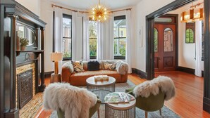 Amplia sala de estar con chimenea, un ventanal con cortinas, una lámpara moderna y una zona de estar acogedora con un sofá y dos sillones.