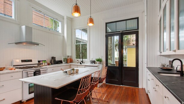 Una cocina moderna con una isla grande, armarios blancos y sillas de cobre.