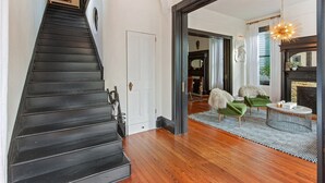 Una escalera que lleva a una habitación con chimenea, un sillón verde y una mesa de centro redonda.