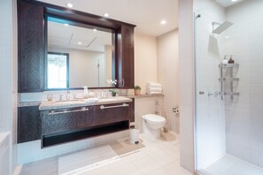 A modern bathroom with a large mirror, dark wood vanity, white tiles, a glass shower enclosure, and a toilet.