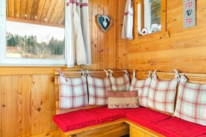 A wooden cabin interior with a bench, plaid cushions, heart-shaped decorations, and a window with a view of trees. - Chalet in Harreberg With Garden Views (Harreberg)