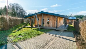 Una cabaña de madera con techo azul, entrada pavimentada y zona verde circundante.