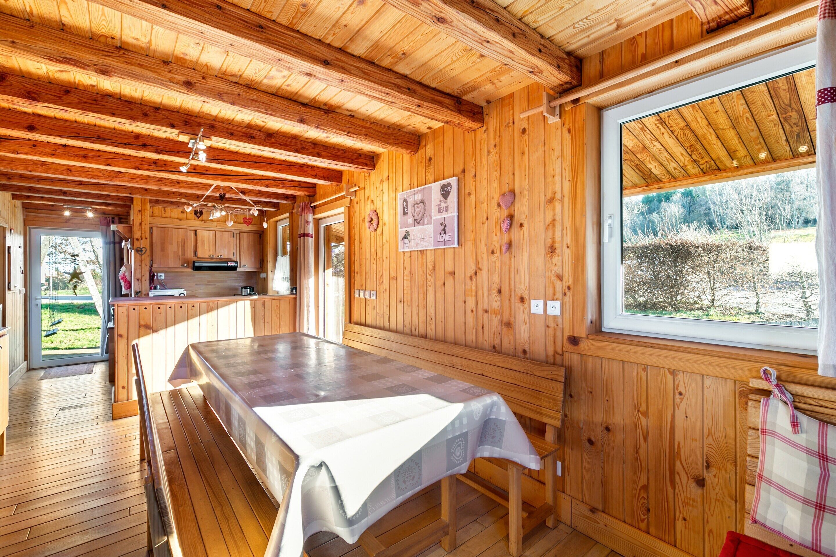 Un interior de fusta amb taula de dinar, armaris de fusta i finestra amb vista a arbres.