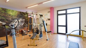 A gym with cardio machines, weightlifting equipment, and a mural of a forest. - Apartment in Tuscany Near Lake Trasimeno (Tuoro sul Trasimeno)