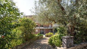 A brick pathway leading to a building with a balcony, surrounded by lush greenery and olive trees. - Apartment in Tuscany Near Lake Trasimeno (Tuoro sul Trasimeno)