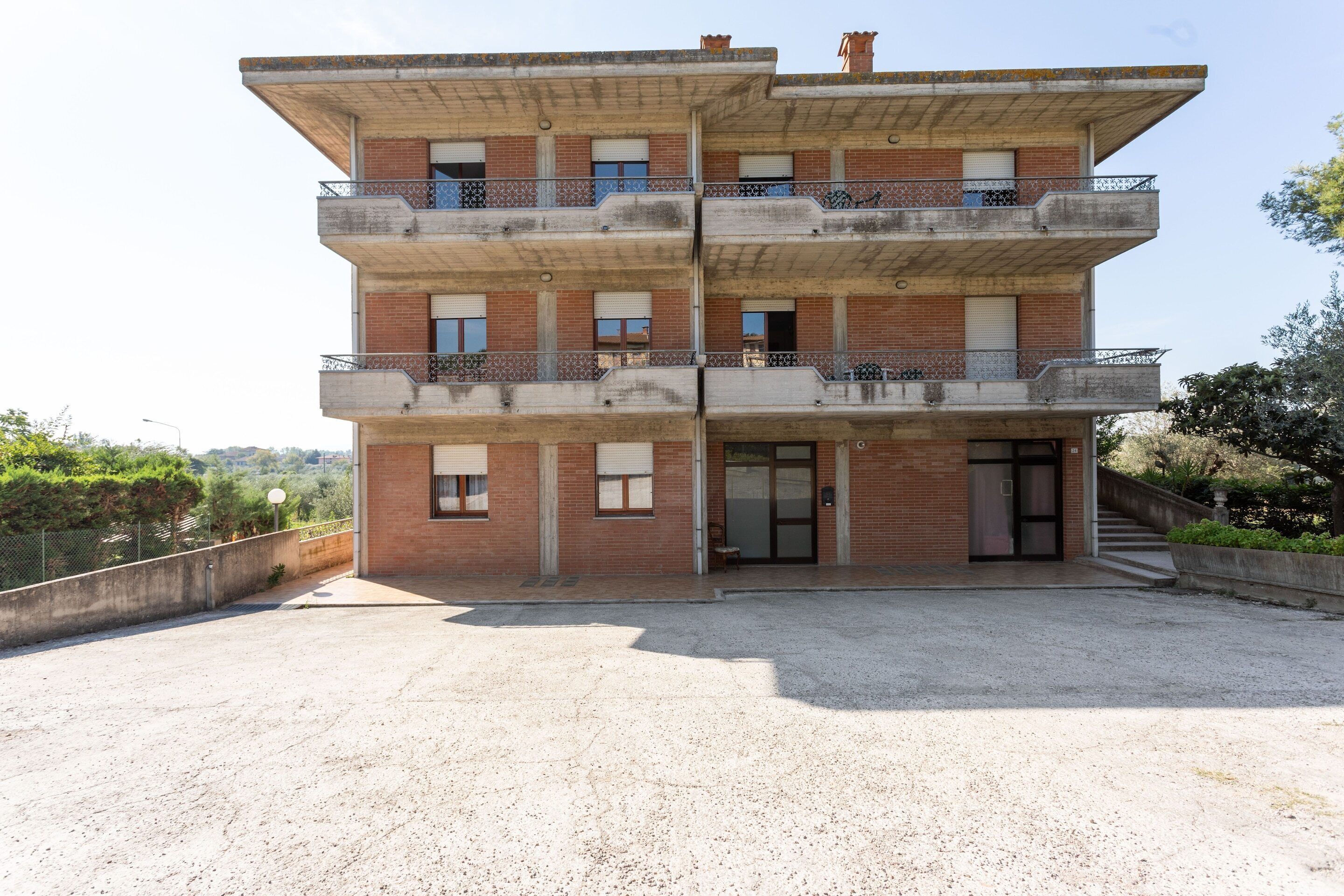 Edifici de diverses plantes amb entrada central, balcons a cada pis i sòl de grava al davant.