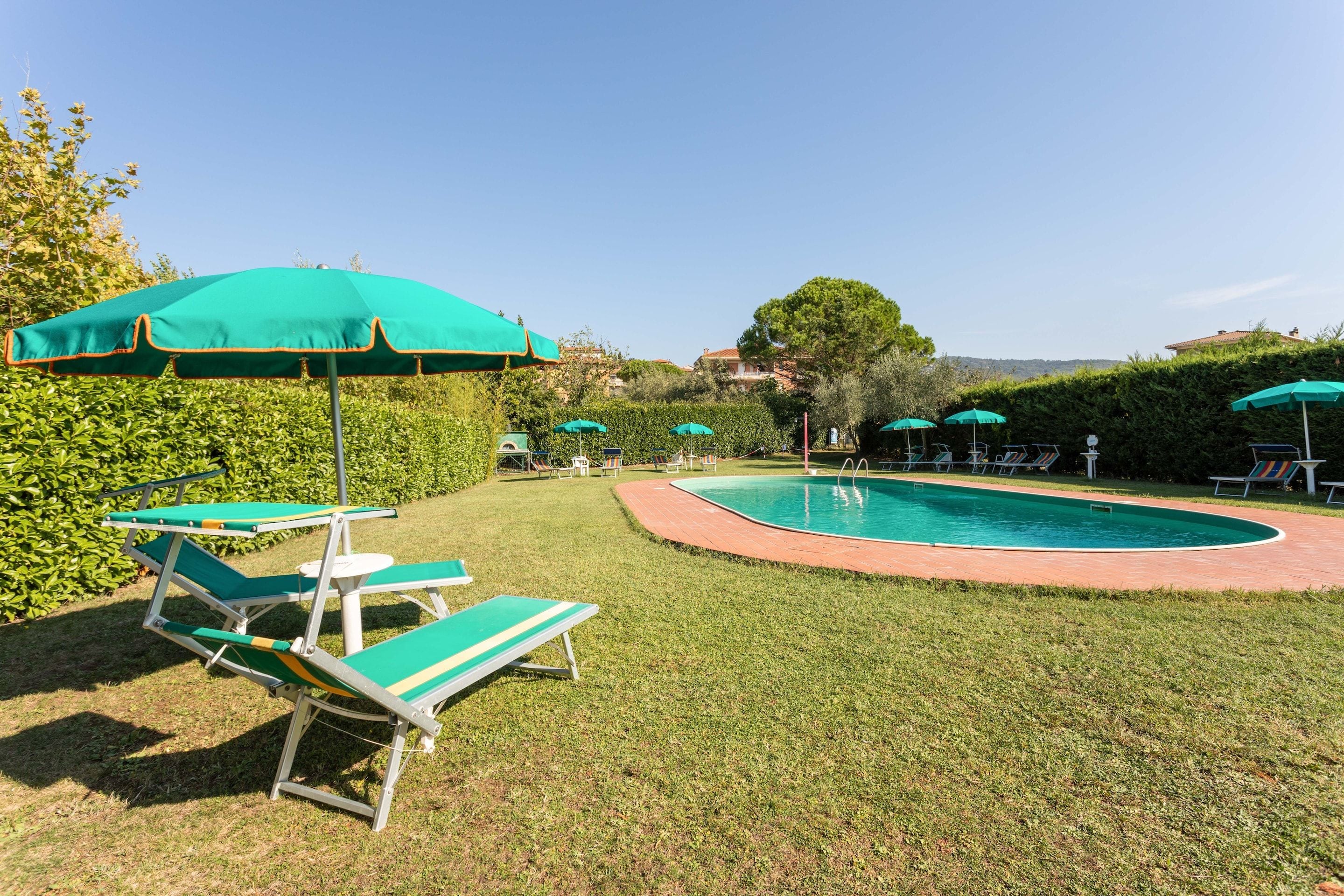Un área de piscina con sombrillas verdes, sillas de descanso y un césped bien cuidado.