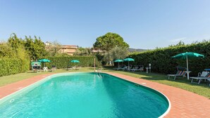 A rectangular swimming pool with a brick border, surrounded by green hedges and trees. - Apartment in Tuscany Near Lake Trasimeno (Tuoro sul Trasimeno)