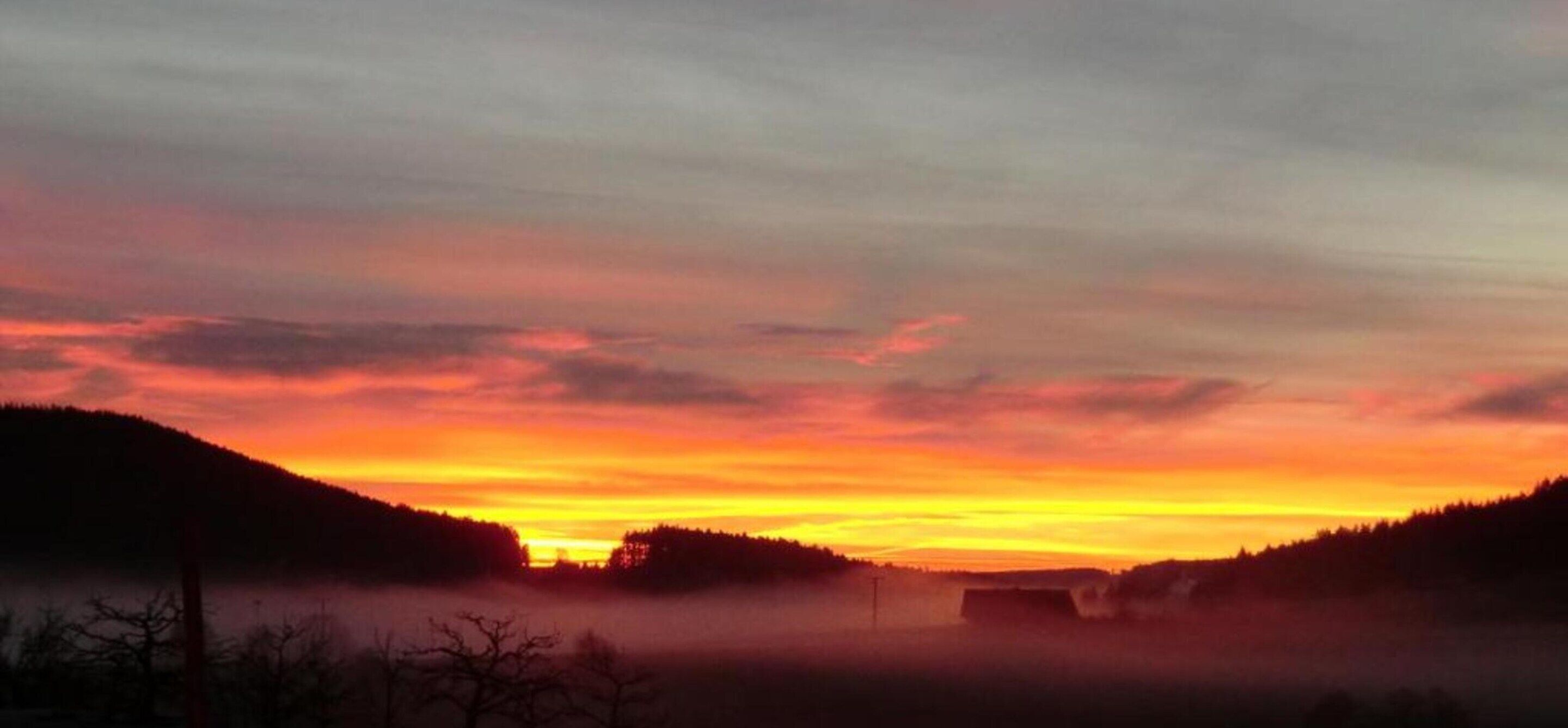 Een zonsondergang boven een heuvellandschap met een mistige voorgrond.