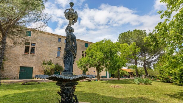 A courtyard with a fountain, a stone building, and trees. - Flat in a Beautiful Building With Pool (Meze)