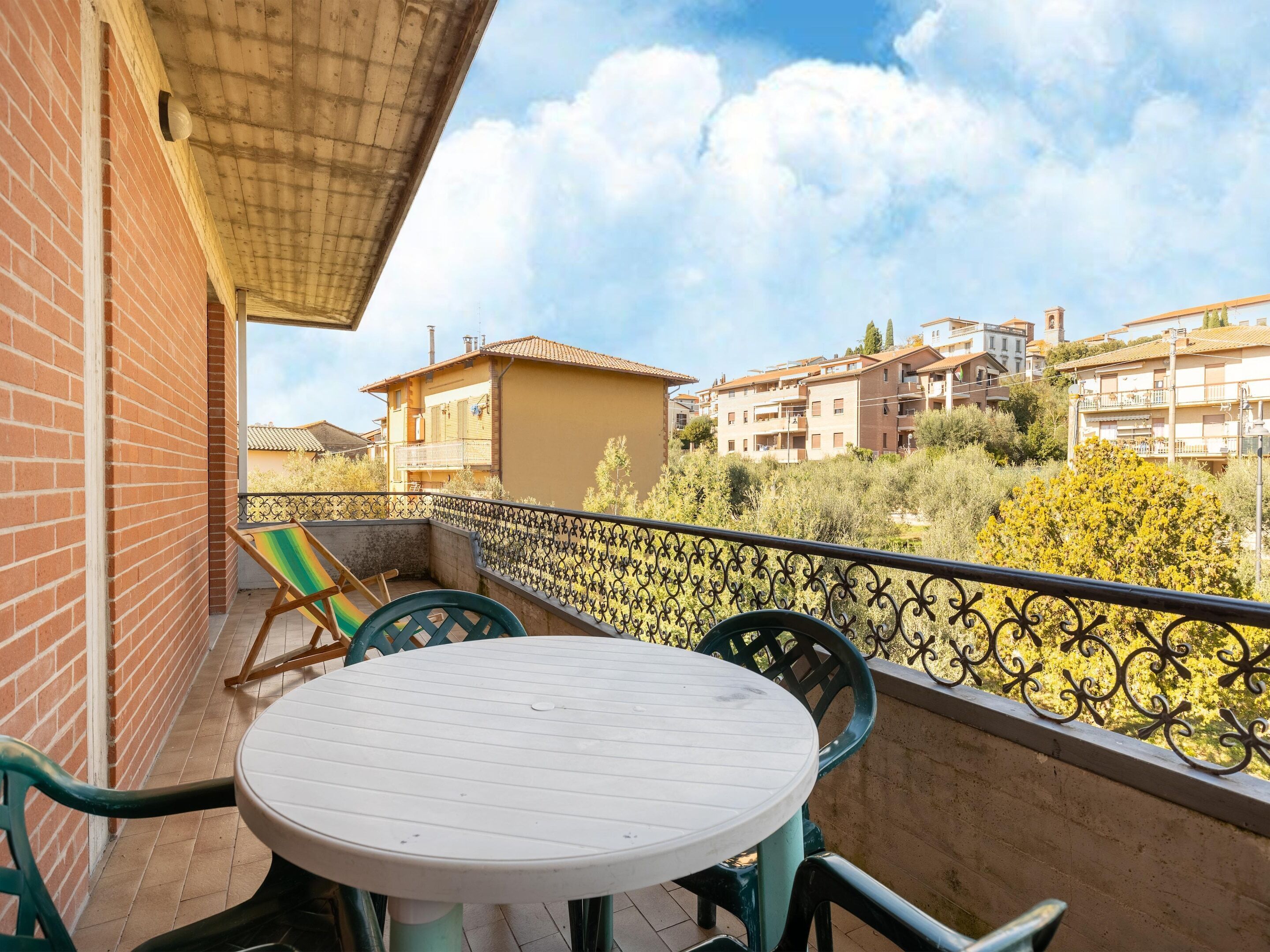 A balcony with a round table and chairs, a view of neighboring buildings, and a metal railing.