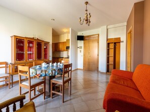 A dining area with a table set for four, wooden chairs, a cabinet with glass doors, and a kitchen in the background.