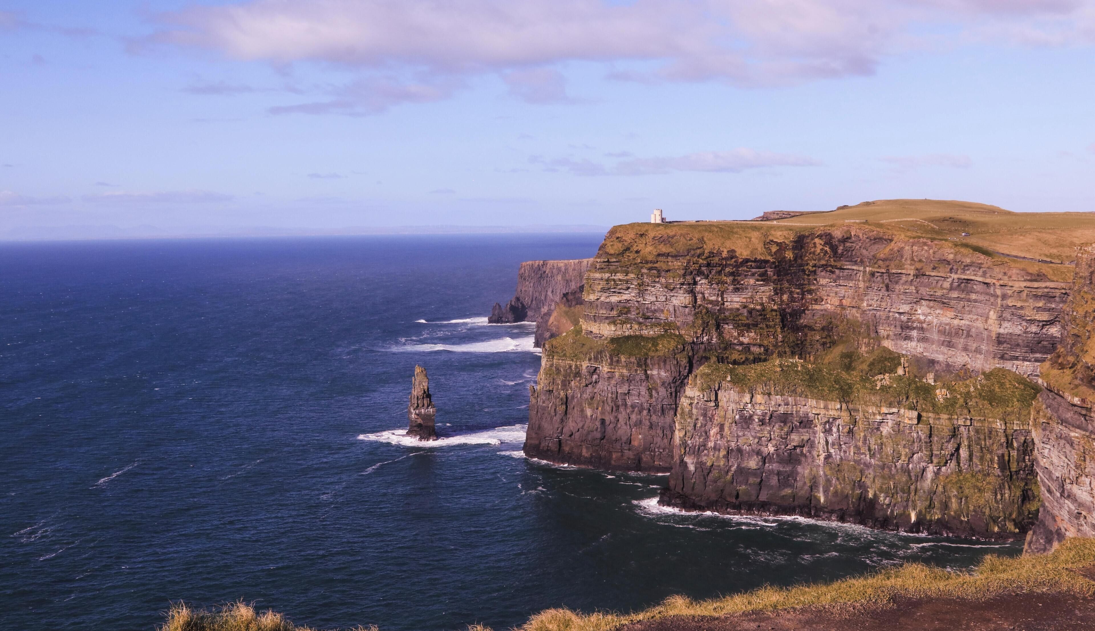 A coastal cliff with a lighthouse, ocean waves, and a clear sky.