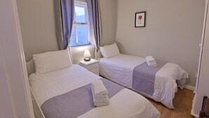 Una stanza con due letti, una finestra con tende, una lampada da comodino e un quadro appeso al muro.
