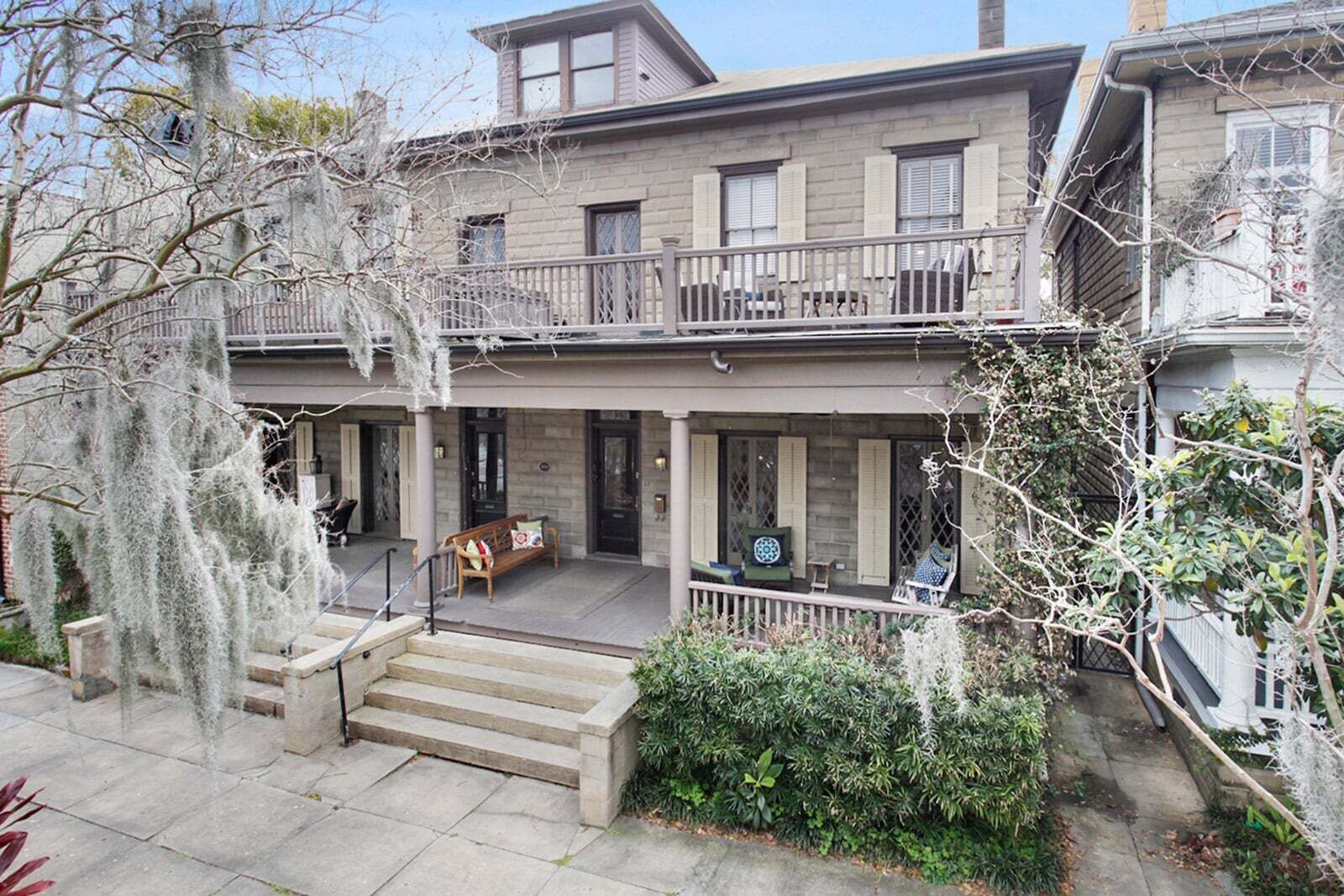 Une maison à deux étages dotée d’un balcon, d’un porche avec un banc et d’un escalier menant à l’entrée.
