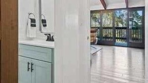 A modern bathroom with a large mirror, light blue cabinets, and a wooden floor.