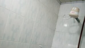 A corner of a room with white tiled walls and a shower area with a white showerhead. - Kilimanjaro Guest House (Nakuru)