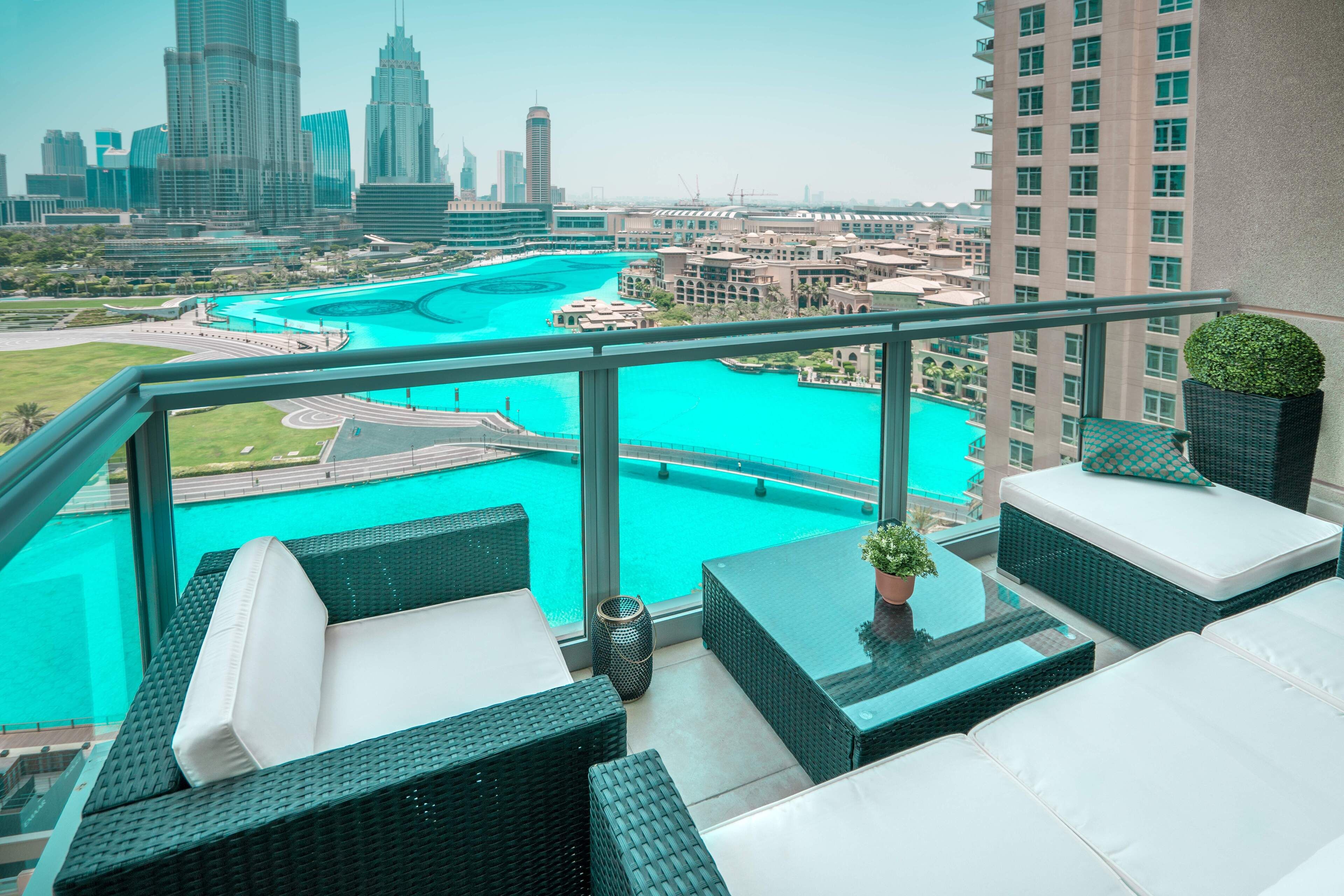A balcony with wicker furniture, a view of a turquoise marina, and modern high-rise buildings in the background.
