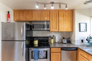 A modern kitchen with stainless steel appliances, wooden cabinets, and a tiled backsplash.