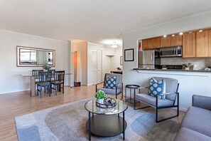 A modern living room with a glass coffee table, grey sofa, and a dining area with a wooden table and chairs.