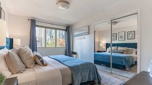 Een slaapkamer met een groot bed, een spiegel en uitzicht op gebouwen.