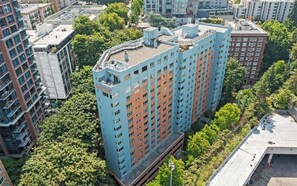A high-rise residential building with multiple floors, surrounded by greenery and other buildings.