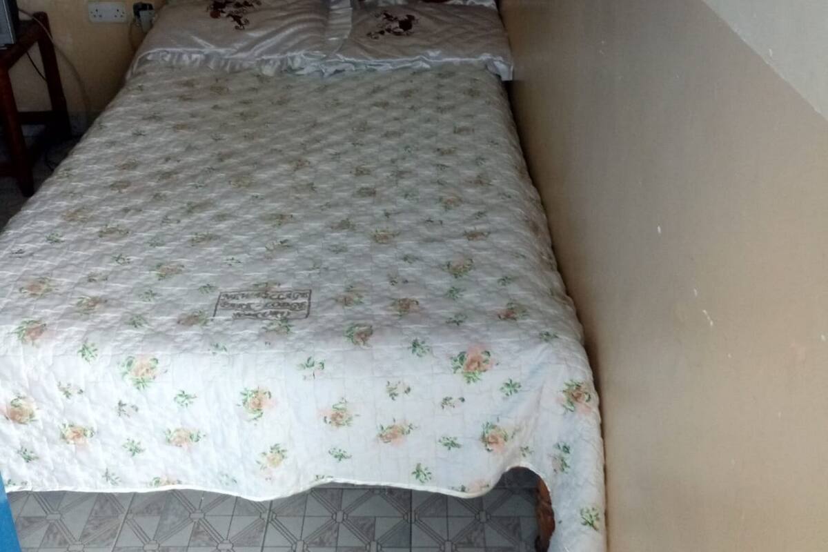 A single bed with a floral bedspread and pillows, a wooden headboard, and a tiled floor.