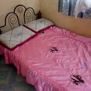 Uma cama com colcha rosa e cabeceira.