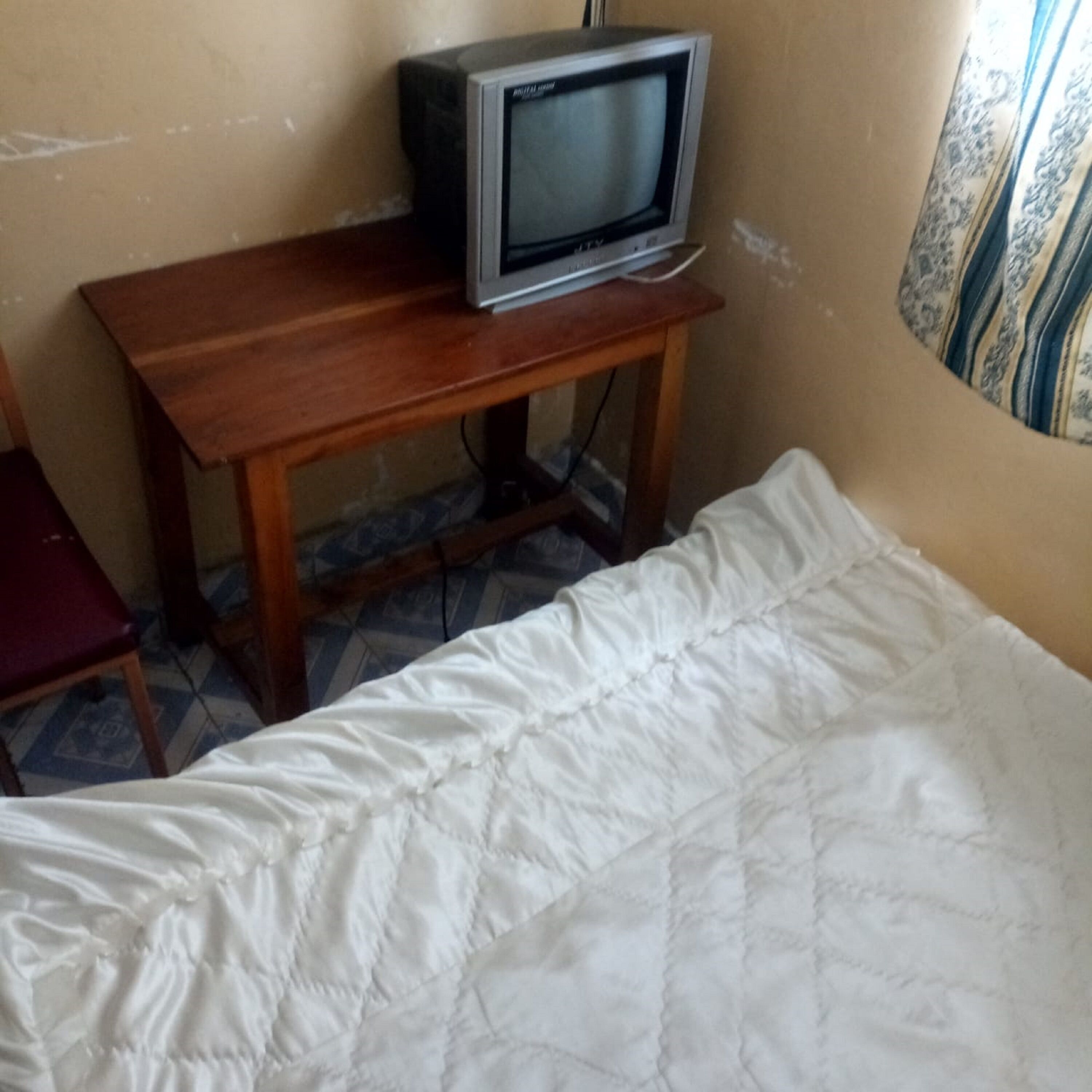 A room with a bed, a wooden table, and a television on top.