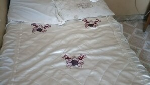A bed with a beige quilt featuring embroidered designs, a white pillow, and a metal headboard.