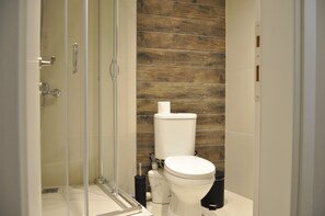 A modern bathroom with a glass shower enclosure, a wooden wall panel, and a white toilet. - Penthouse Apartments, The Luxury Suites (Thessaloniki)