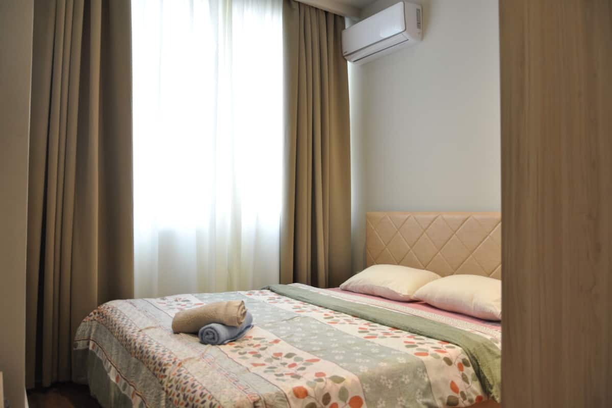 A neatly made bed with a quilt, pillows, and a rolled towel.