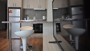 A modern kitchen with two white bar stools, a built-in dishwasher, and a double-door refrigerator.