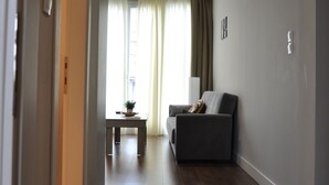 A hallway with a wooden floor leading to a living area with a sofa and a small table.