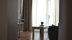 A modern living room with a dining table, a potted plant, and a view through sheer curtains.