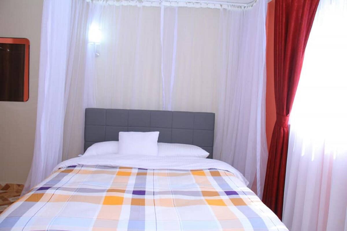 A hotel room with a bed, white curtains, and a red curtain on the right.