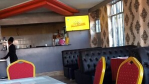 Un restaurant dont la salle à manger est décorée de chaises rouges à cadre jaune, d’une table blanche et dont on aperçoit la cuisine au fond.