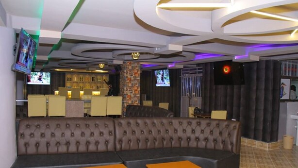 Un espace lounge moderne comprenant un grand canapé d’angle, de petites tables et un bar équipé de plusieurs écrans.
