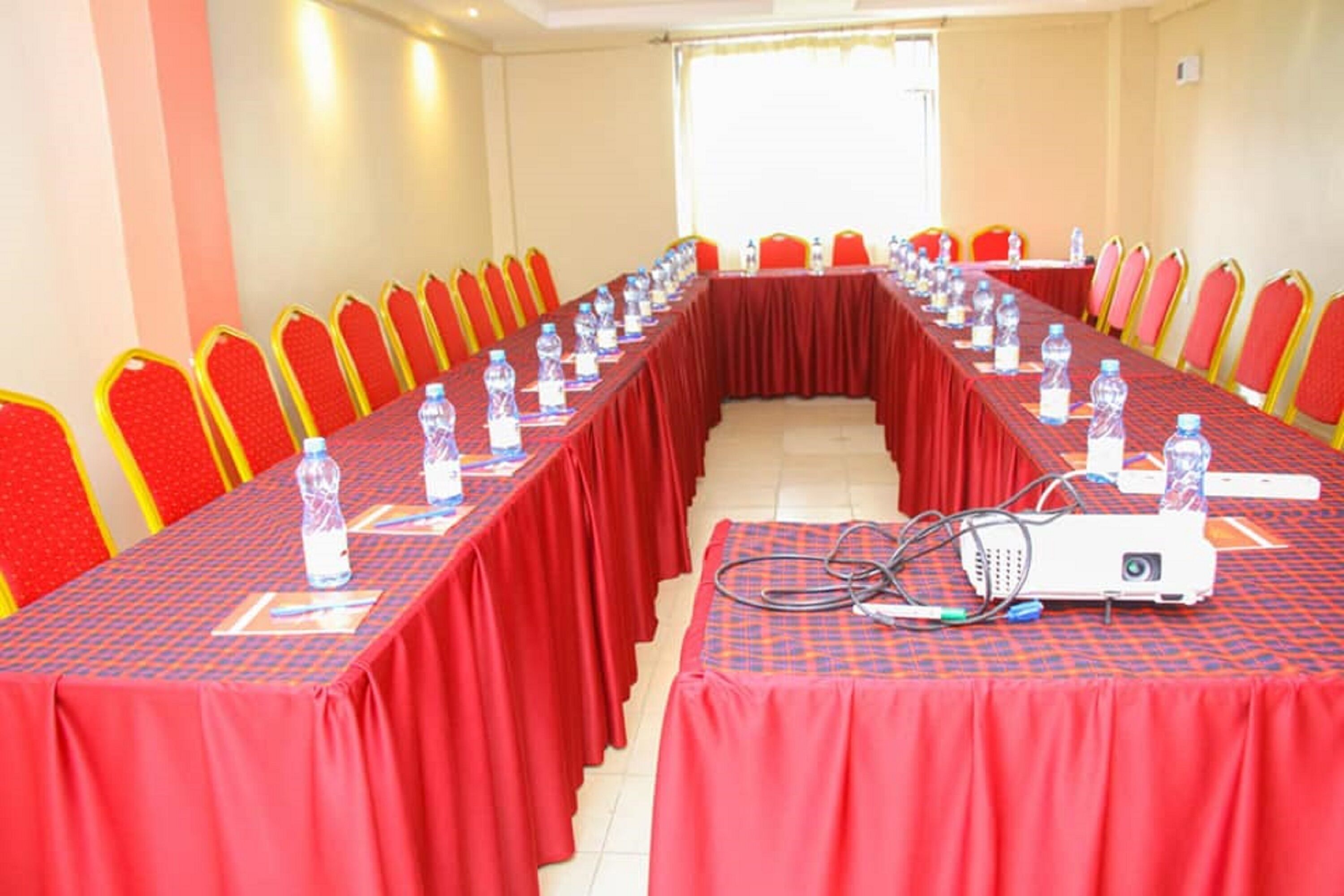 A conference room with a long table, red chairs, water bottles, and a projector.
